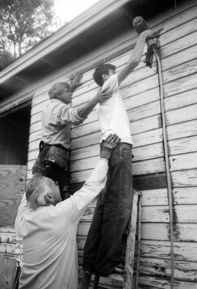 Three generations of the Nash family repairing siding on a Houston house
